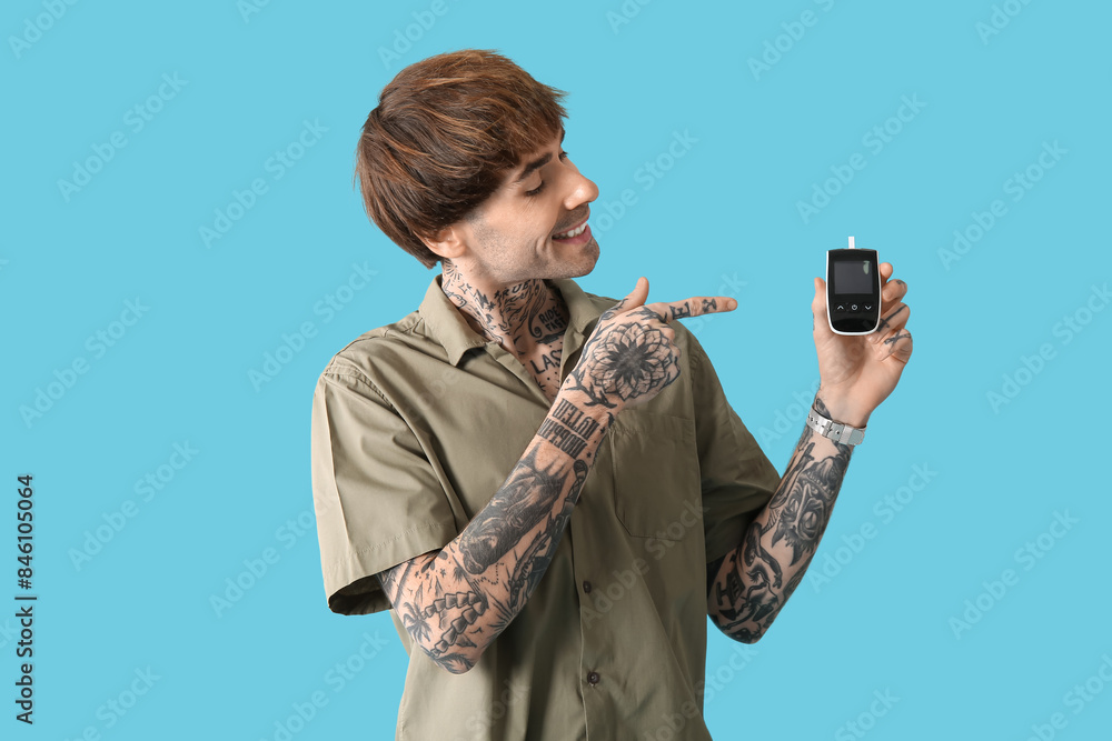 Diabetic young man pointing at glucometer on blue background