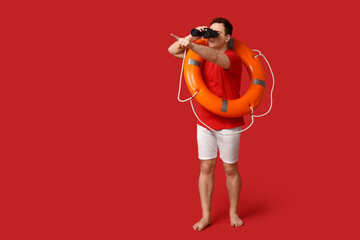 Canvas Print - Male lifeguard with ring buoy looking through binoculars on red background