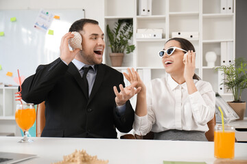 Poster - Happy office workers sitting at table and listening seashells in office. Summer vacation concept