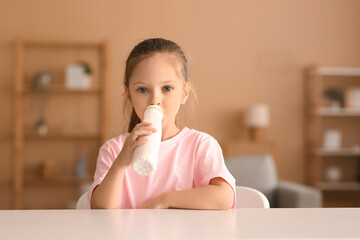 Canvas Print - Cute little girl sitting by table and drinking yogurt at home