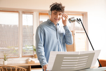 Wall Mural - Handsome young man in headphones with microphone playing synthesizer at home