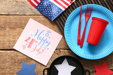 Wall Mural - Composition with greeting card for Independence Day celebration, dinnerware and barbecue utensils on wooden background