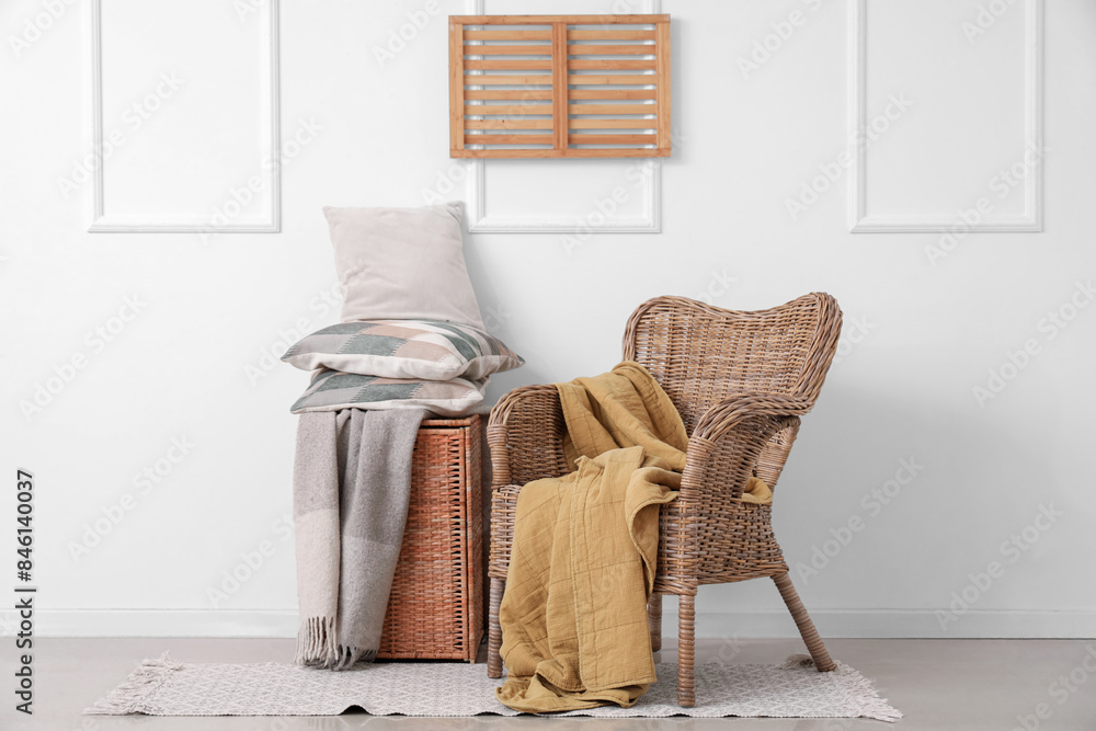 Wicker armchair and basket with stack of pillows near white wall