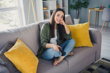 Wall Mural - Full length portrait of nice young girl sit sofa hold controller wear green shirt modern interior flat indoors