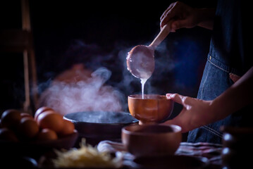 a porridge shop at night on the side of the road as the cook uses a wooden ladle to scoop porridge i