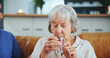 © peopleimages.com - Senior woman, nurse and glass for drinking water on sofa with thirst, medicine and wellness in living room. People, caregiver and elderly patient with health, detox and gut health on couch in house