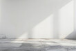 © BOW_NAPASORN - A large empty room with a white wall and a grey floor. The room is very bare and empty, with no furniture or decorations. The sunlight coming in through the window casts a shadow on the floor