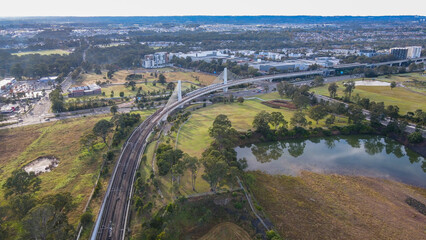 Sticker - Aerial drone view of a train heading toward Rouse Hill Station on the metro northwest railway line, Greater Sydney, NSW Australia crossing the railway bridge in June 2024 