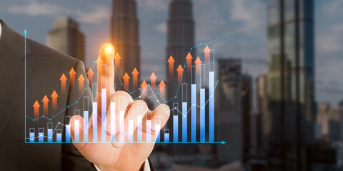 Wall Mural - Close up of businessman hand pointing at growing business graph on blurry city background. Financial growth and technology concept. Double exposure.