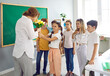 © Studio Romantic - Children students giving flowers to their teacher at elementary school congratulating her on the holiday. They are smiling and looking at her in classroom. Good attitude, care and respect concept.