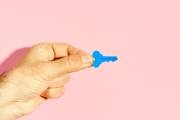 Man's hand holding blue key against pink background