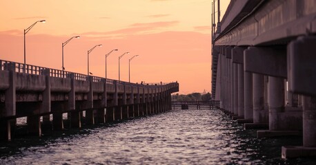 Wall Mural - Scenic view of a bridge over water during sunset with street lights illuminating the path.