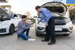 © chadchai - Two individual inspect damage on a vehicle. Car’s owner pointing at a dent on the bumper of the car. An insurance staff taking picture with smartphone, conducting an assessment related to the damage.