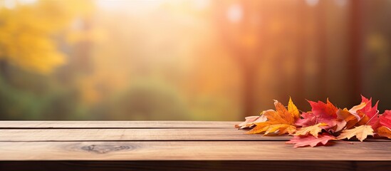 Poster - Autumn-themed wooden table with a blurred red and yellow leaves background sets the scene for a copy space image.