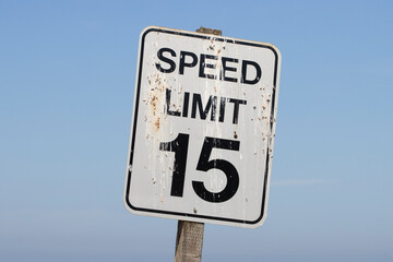 Closeup of a 15-mile speed limit sign covered with bird droppings, isolated against a blue sky background.