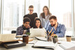 © Prostock-studio - Multiethnic group of individuals gathered in an office setting, all focused on the screen of a laptop. They appear engaged and attentive as they discuss the content displayed on the device.