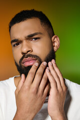 Wall Mural - A close-up of a young man with a beard performing his skincare routine.