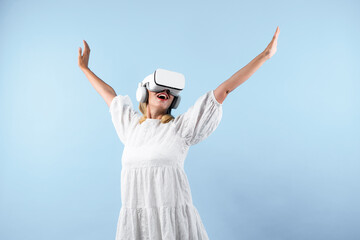 Wall Mural - Caucasian girl enter metaverse while spread arms with relax at blue background. Excited woman enjoy playing game by using VR goggles with blue background. Innovation technology concept. Contraption.
