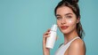© Prostock-studio - A woman with brown hair is applying white face cream to her cheek. She is smiling and looking at the camera. The background is a light blue color.