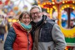 © Markus Schröder - Portrait of a jovial couple in their 50s dressed in a thermal insulation vest isolated on lively amusement park background