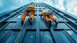 © familymedia - Two workers in orange overalls and helmets climb a blue building facade with ropes and equipment
