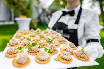 Close-up view of a tray with neatly arranged canapés held by a person in a black and white uniform, suggesting a catering service at an event