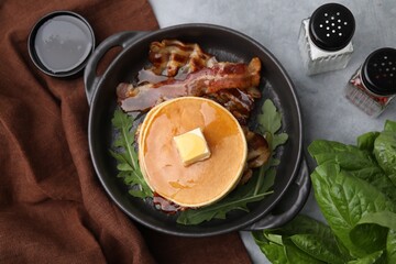 Wall Mural - Tasty pancakes with butter, fried bacon and fresh arugula on grey table, flat lay