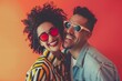 © Markus Schröder - Portrait of a joyful latino couple in their 30s wearing a trendy sunglasses while standing against solid color backdrop