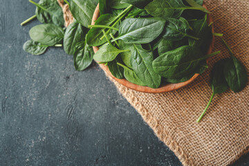 Wall Mural - Fresh organic spinach leaves in a wooden bowl over dark rustic background. Top view with copy space