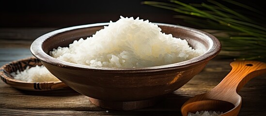 Wall Mural - Wooden spoon resting beside a bowl of rice on a tabletop, showcasing Chinese cooking with soaked sticky rice. with copy space image. Place for adding text or design