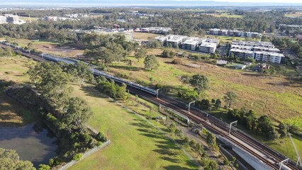 Sticker - Aerial drone rotating reverse view of a train coming from Tallawong before crossing the railway bridge as it arrives at Rouse Hill Station on the metro northwest railway line, Greater Sydney, NSW Aust