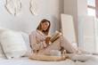 © mary_markevich - pretty smiling woman relaxing at home on bed in morning in pajamas reading book