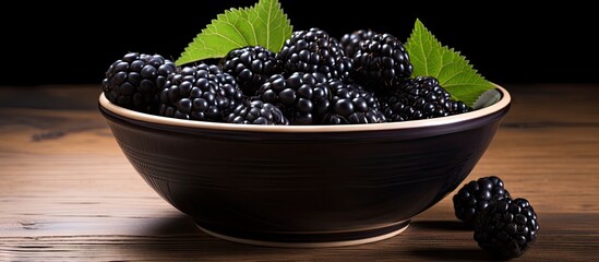 Poster - Blackberries with green leaves arranged in a bowl placed on a wooden table. with copy space image. Place for adding text or design