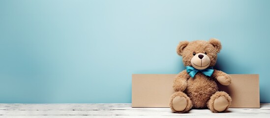 Cute teddy bear positioned on top of a cardboard box with a blank blue label sign nearby. with copy space image. Place for adding text or design