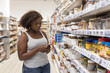 © Anna Berkut/Stocksy - curvy woman in grocery store or supermarket checking her smart phone