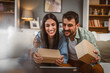 © Miljan Živković - Couple open birthday gift together via video call on tablet at home