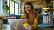 © Leafart - Happy smiling young woman holding a credit card and laptop doing online shopping at home