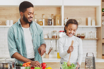 Wall Mural - Cute little african girl helping her dad to make salad, cooking together, kitchen interior, copy space