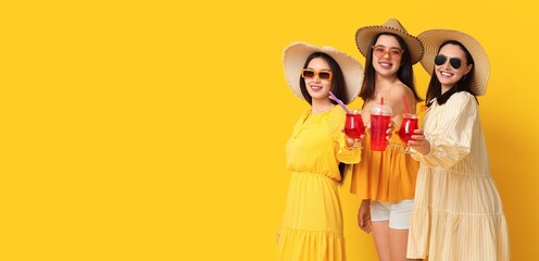 Poster - Beautiful young women in beach hats and with glasses of cocktail on yellow background with space for text