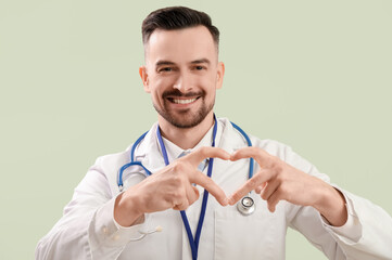 Wall Mural - Male doctor making heart with his hands on green background, closeup