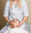 © BY-_-BY - Young woman enjoying facial massage, lying on spa bed indoor at beauty salon.