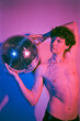 © Viktor Solomin/Stocksy - Handsome topless man with disco ball in pink neon light