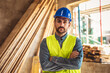 © Mediteraneo - Portrait of Construction site manager standing  wearing safety vest and helmet, thinking at construction site. Young architect watching construction site with confidence.