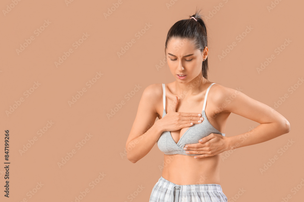 Young woman checking her breast on beige background. Cancer awareness concept