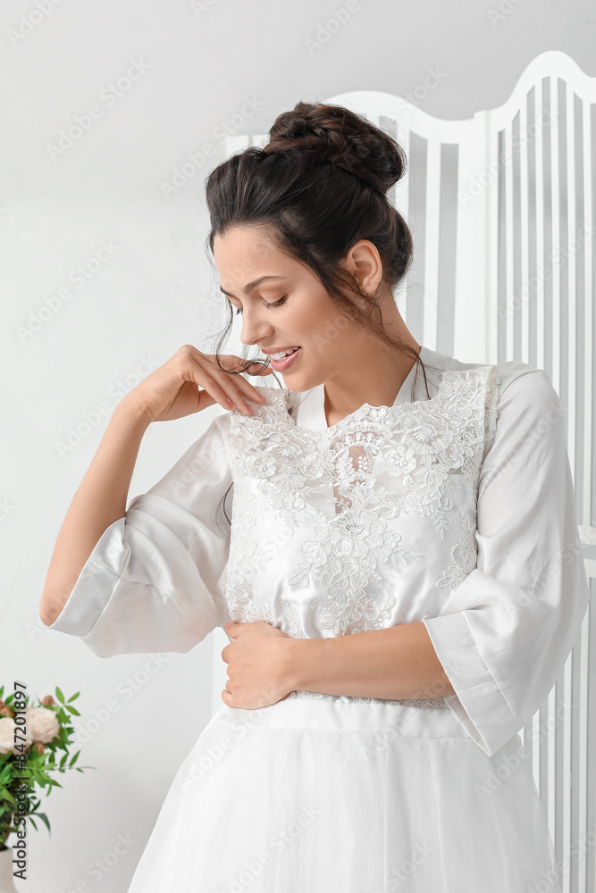 Young bride trying on her wedding dress in bedroom