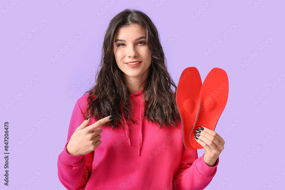 Young woman pointing at orthopedic insoles on lilac background