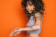 © VICTOR TORRES/Stocksy - Joyful tattooed woman with curly hair on orange background