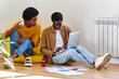 © Guille Faingold/Stocksy - Colleagues at home using laptop sitting on the floor.
