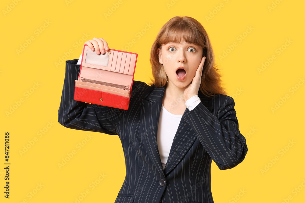 Surprised young woman holding empty wallet on yellow background