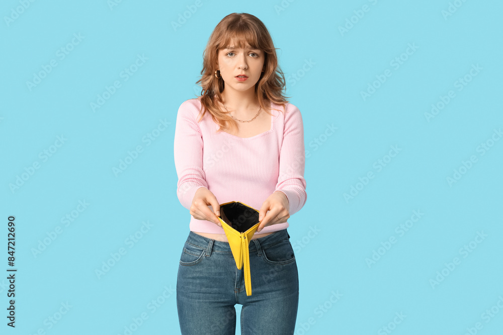 Beautiful young woman holding empty yellow wallet on blue background